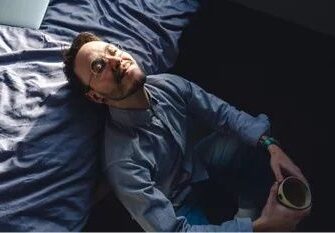 Entspannter Mann liegt mit Tasse auf einem zerwühlten Bett