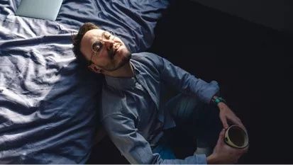 Entspannter Mann liegt mit Tasse auf einem zerwühlten Bett