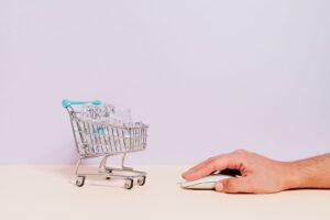 Hand bedient eine Maus neben Einkaufswagen mit Glaswaren