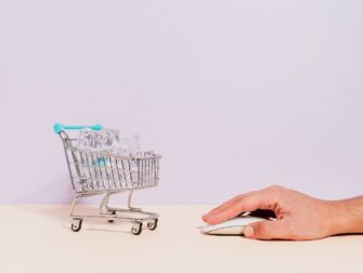 Hand bedient eine Maus neben Einkaufswagen mit Glaswaren