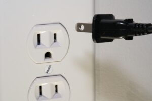 Schwarzer Netzstecker neben einer ungenutzten Doppelsteckdose
