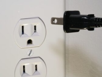 Schwarzer Netzstecker neben einer ungenutzten Doppelsteckdose