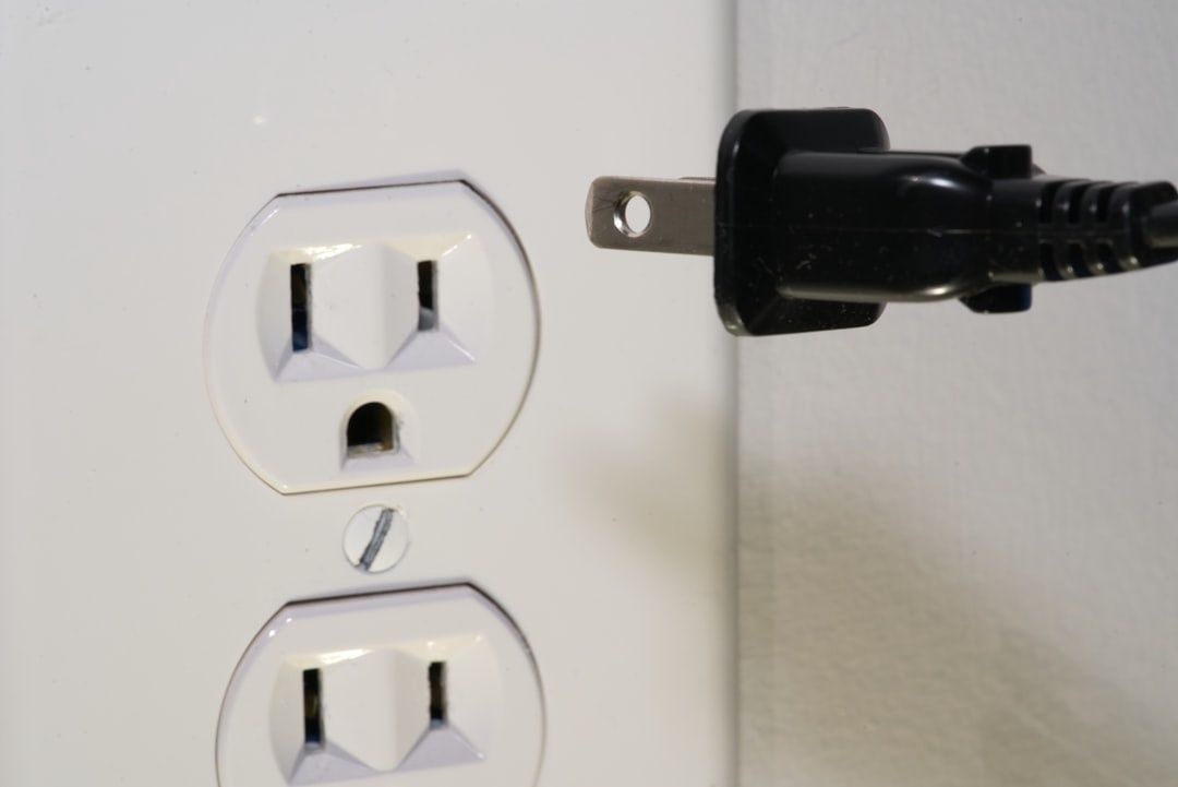 Schwarzer Netzstecker neben einer ungenutzten Doppelsteckdose