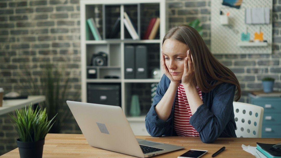 Gestresste Frau sitzt vor einem Laptop und hält sich die Schläfen